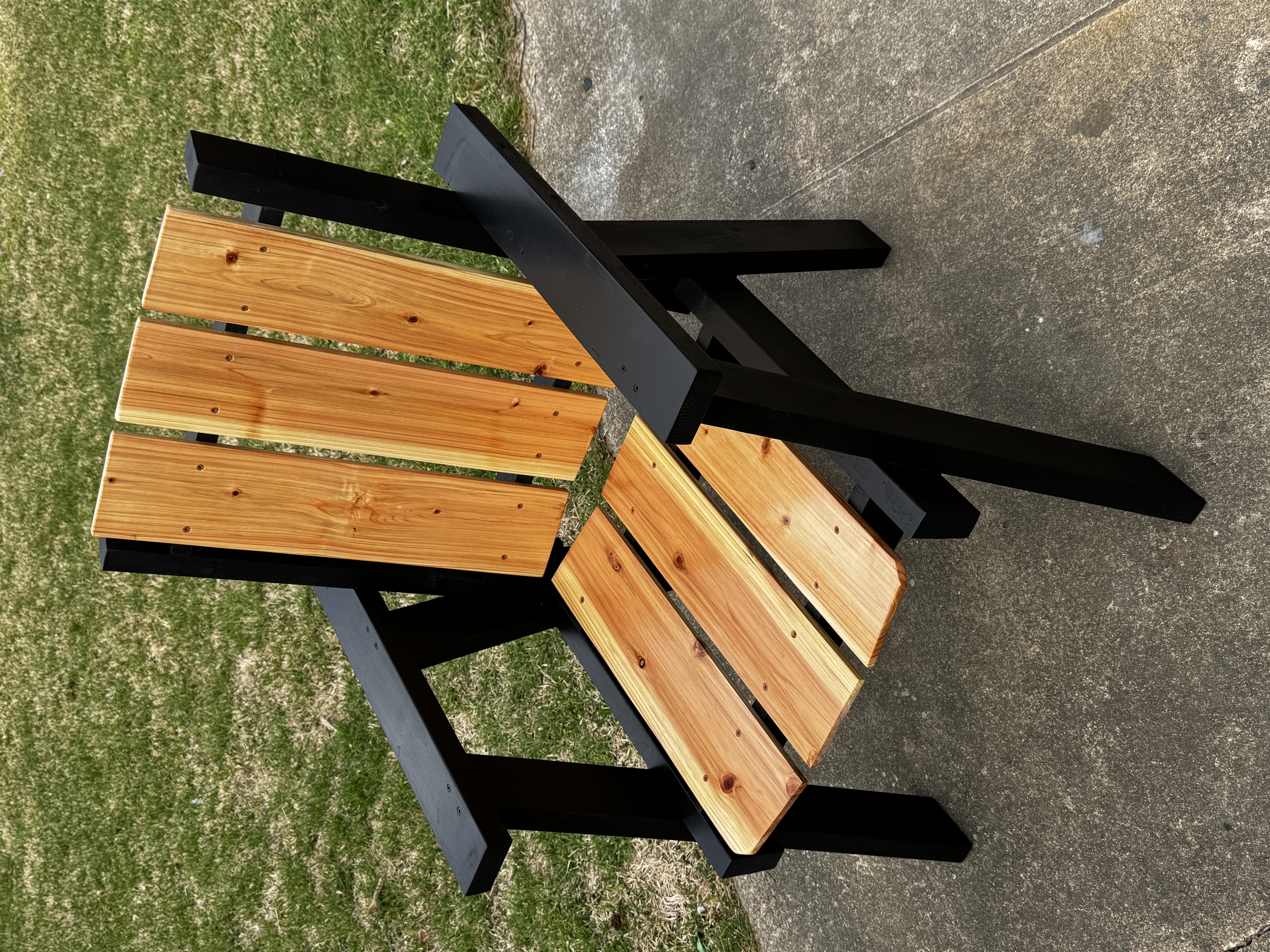 Black-frame chair with cedar seat and backrest on grass and concrete